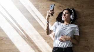 Junge Frau mit Kopfhörern blickt auf ihr Smartphone