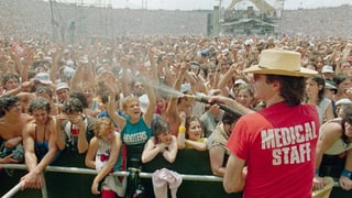 Ein Mann mit einem T-Shirt Medical Staff spritzt Wasser in eine riesige Publikumsmenge. Ein Mann mit einem T-Shirt Medical Staff spritzt Wasser in eine riesige Publikumsmenge.