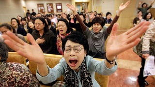 Eine Frau mit geschlossenen Augen streckt beide Arme in die Luft und betet mit offenem Mund. Eine Frau mit geschlossenen Augen streckt beide Arme in die Luft und betet mit offenem Mund.