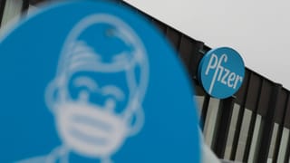 Gebäude mit Logo Pfizer. Davor ein Schild, das Maskenpflicht anzeigt. Gebäude mit Logo Pfizer. Davor ein Schild, das Maskenpflicht anzeigt.