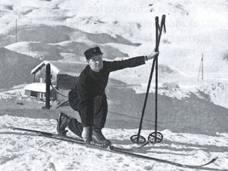 Schwarz-weiss Aufnahme von Arnold Lunn, der sich die Ski anzieht. 