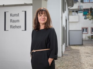 Eine Frau im schwarzen Kleid steht vor einem Gebäude mit der Schrift «Kunst Raum Riehen».