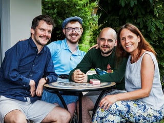 Die drei Protagonisten sitzen zusammen mit Renato an einem Gartentisch.