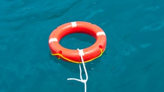 Ein roter Rettungsring mit weissen Streifen treibt an einem Seil im Wasser. Ein roter Rettungsring mit weissen Streifen treibt an einem Seil im Wasser.