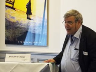 Mit grauen Haar und Brille auf einem Podium, Publikumsfragen beantwortend. Mit grauen Haar und Brille auf einem Podium, Publikumsfragen beantwortend.