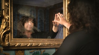 Eine Frau guckt in einen alten Spiegel.