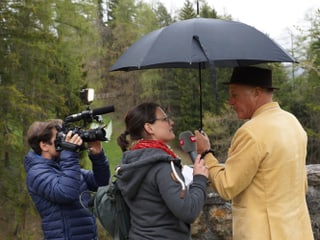 Ein Kamermann, eine Reporterin und ein Interviewpartner unter einem Regenschirm.