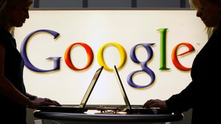 Zwei Frauen arbeiten stehend an ihren Notebooks vor einem Google-Logo. Zwei Frauen arbeiten stehend an ihren Notebooks vor einem Google-Logo.
