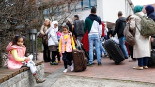 Migranten mit Koffern vor einem grossen Gebäude in Deutschland.