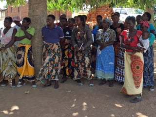 Frauen stehen auf dem Dorfplatz unter einem Baum in einer Reihe