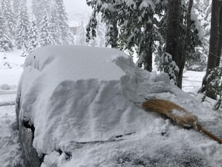 Auf einem Auto liegt noch viel Schnee und ein Besen, der beim Abräumen hilft.