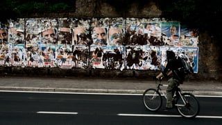 Ein Fahrradfahrer fährt an einer Wand mit Wahlplakaten entlang.