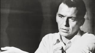 Frank Sinatra bindet sich mit Krawatte den Arm ab.