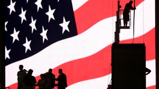 Riesige US-Flagge, davor die Silhouetten von Menschen