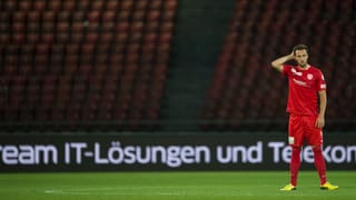 Ein Spieler steht alleine auf dem Rasen, im Hintergrund eine leere Tribüne.