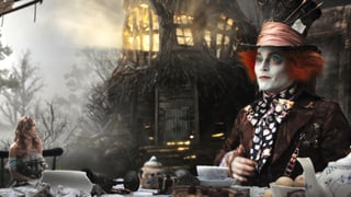 Eine Frau und ein Mann sitzen zum Tee in einer skurrilen Umgebung an einem Tisch. Die Frau ist winzig klein, der Mann erscheint riesig. Der Mann trägt einen Hut und hat rot gefärbte Haare. Die Augen stechen durch ihre giftgrüne Farbe hervor.