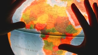 Zwei Hände auf einem erleuchteten Globus, der Afrika zeigt. 