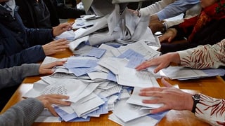 Ein Tisch voll mit Wahllisten und Hände, die nach ihnen greifen.