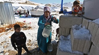 Eine Frau füllt Wasser in einen Behälter in einem Flüchtlingslager, der Boden ist schneebedeckt.