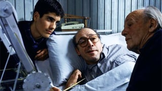 Ramon liegt im Krankenbett, neben ihm sitzen sein Sohn, der einen Federkiel hält, und sein Vater.