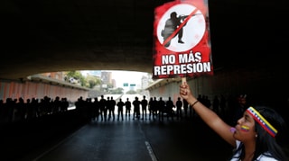 Frau mit einem Plakat gegen Repression, im Hintergrund Polizisten