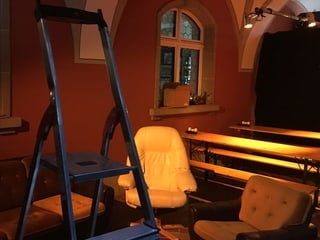 dunkler Raum mit Bänken und zwei Polsterstühlen und Leiter dunkler Raum mit Bänken und zwei Polsterstühlen und Leiter