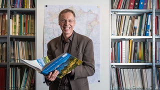 Raimund Rodewald steht mit einem Buch in seinem Büro.