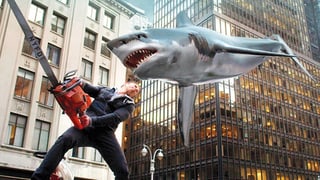 Ein Mann schwingt eine grosse Kettensäge gegen einen heranfliegenden Riesenhai.