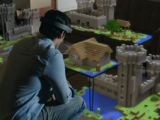 Mann sitzt vor einem Tisch, darauf ein virtuelles Schloss aus Bausteinen.