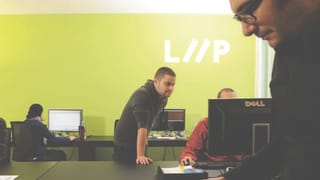 LIIP-Mitarbeitende sitzen und stehen an PCs vor einer grün gestrichenen Wand mit dem Firmenlogo. LIIP-Mitarbeitende sitzen und stehen an PCs vor einer grün gestrichenen Wand mit dem Firmenlogo.