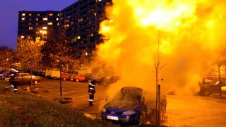 Ein brennendes Auto steht vor einem Wohnblock.