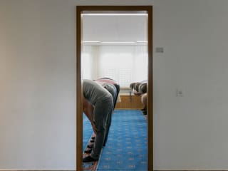 Durch eine offene Tür sieht man in den Gebetsraum. Drinnen stehen mehrere Männer, die ihren Oberkörer beugen. Durch eine offene Tür sieht man in den Gebetsraum. Drinnen stehen mehrere Männer, die ihren Oberkörer beugen.