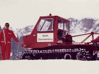 Mann in rotem Ski-Anzug steht neben einem Ratrac.