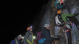 Bergsteiger im nächtlichen Dunkel stehen Schlange vor einer Steilwand.