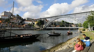 Paar am Ufer eines Flusses. Dahinter die Brücke von Porto.