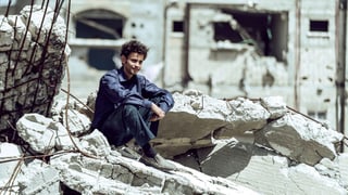 Ein Junge sitzt auf einem Trümmerhaufen.