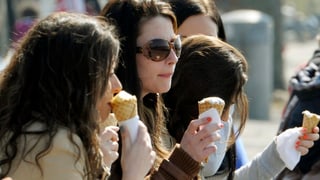 Drei Frauen essen bei sommerlichen Temperaturen ein Glace auf einer Bank.