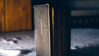 Ein Buch mit einem Kreuz steht auf einem Tuch.