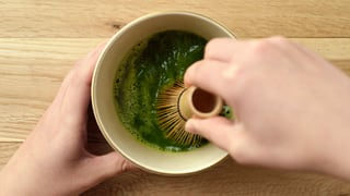 Eine Hand hält eine Teeschale, die andere schlägt den Tee mit einem Bambusbesen schaumig. Eine Hand hält eine Teeschale, die andere schlägt den Tee mit einem Bambusbesen schaumig.