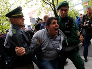 Zwei Polizisten halten eine wütende Demonstrantin fest.