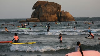 Chinesische Touristen surfen an einem Strand in Hainan.