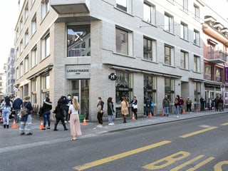 Eine Schlange von Menschen steht entlang einer Strasse bis um eine Hausecke. Eine Schlange von Menschen steht entlang einer Strasse bis um eine Hausecke.