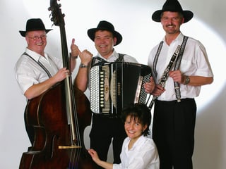 Drei Musiker und eine Musikerin in weissen Hemden und schwarzen Hosen. Instrumente: Kontrabass, Akkordeon, Klarinette.