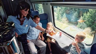 Eine Angestellte der Minibar gibt einem Kind ein Pack Chips in einem Zug