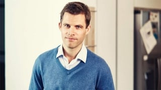 Ein junger Mann mit kurzen braunen Haaren, mit blauem Pullover und weissem Hemd darunter schaut in die Kamera Ein junger Mann mit kurzen braunen Haaren, mit blauem Pullover und weissem Hemd darunter schaut in die Kamera