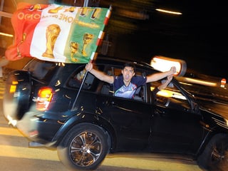 Ein Fan lehnt sich auf dem Rücksitz schreiend aus dem Fenster und trägt die italienische Flagge in der Hand.