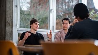 Drei junge Männer an einem tisch. Einer gestikuliert mit den Händen. Drei junge Männer an einem tisch. Einer gestikuliert mit den Händen.
