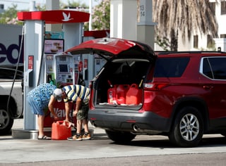 Zwei Menschen füllen an einer Tankstelle Benzin in Behälter. Das Auto voller Behälter.