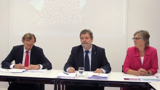 Eine Frau und zwei Männer an einer Medienkonferenz.