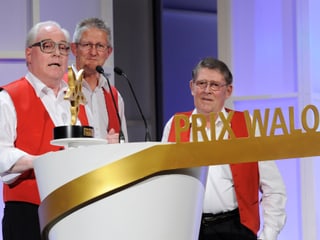 Die drei Musiker der Kapelle am Rednerpult mit der PRIX WALO-Auszeichnung.